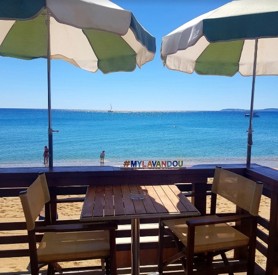 Terrasse de L'Effet Mer face à la plage : parasols vert et blanc, sable et mer turquoise du Lavandou
